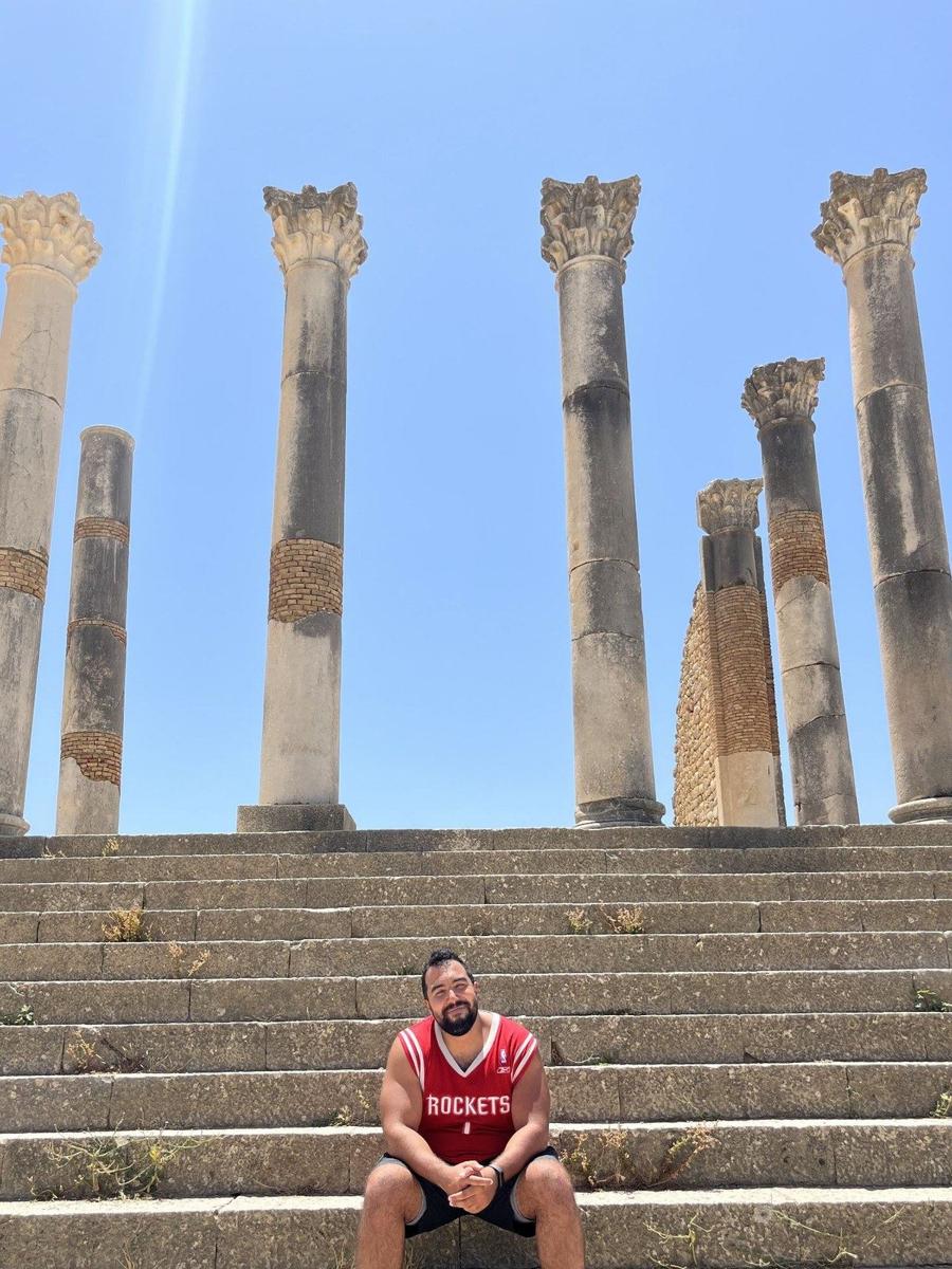 Younes assis sur les marches devant les colonnes antiques de Volubilis, au Maroc